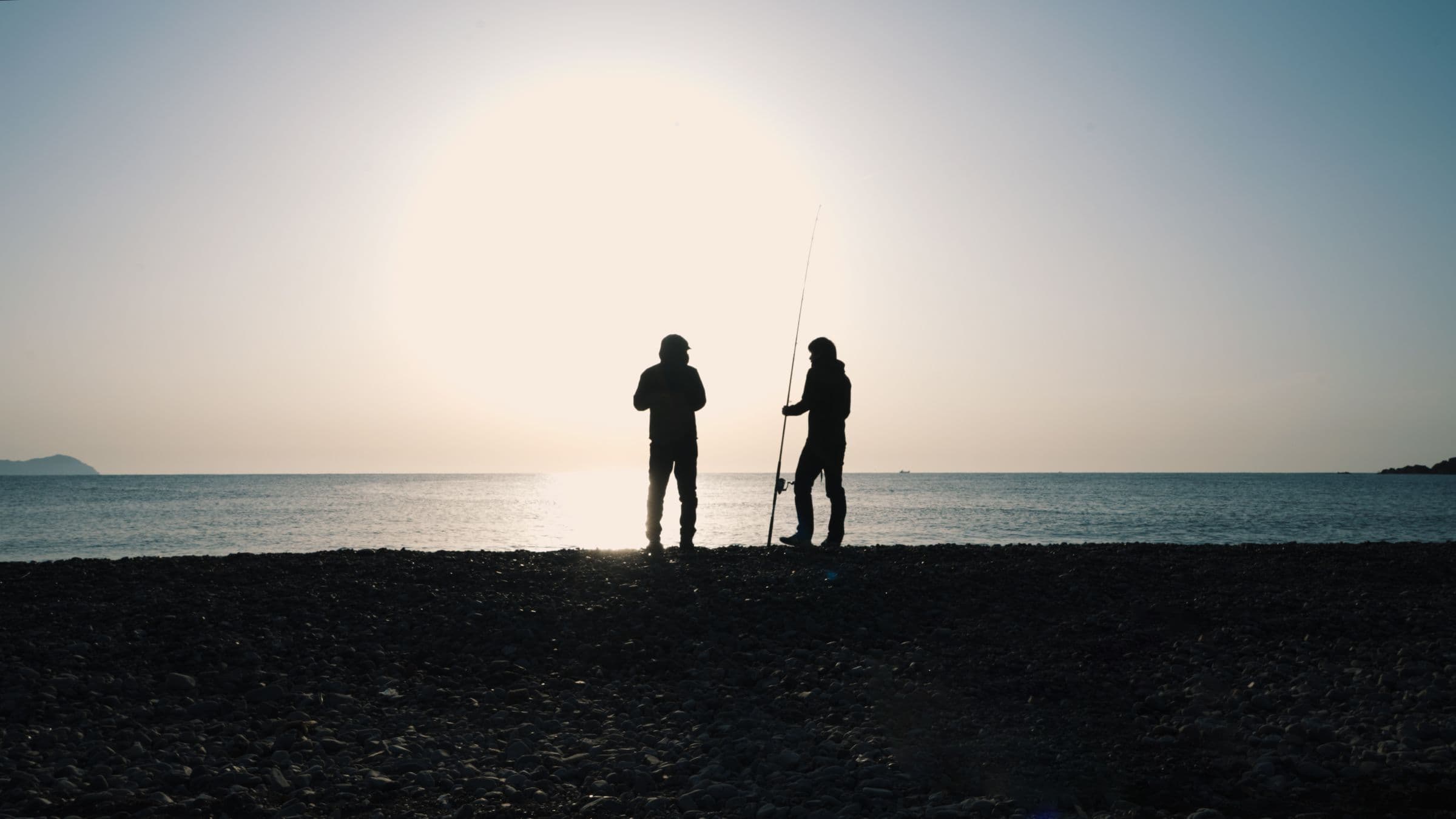夕暮れの海辺で並んで釣りをする二人のアングラー